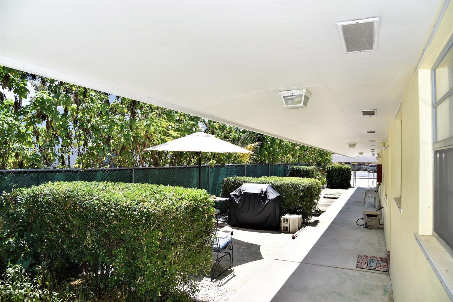 A covered patio features a grill, outdoor furniture, and a hedge-lined fence — 1008 N 18  AVENUE, Lake Worth FL 33460, LAKE WORTH, FL