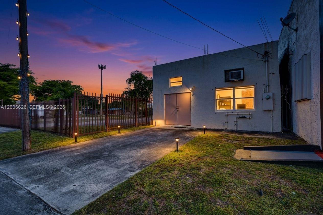 A concrete building exterior with a metal gate and a small paved driveway at dusk — 4167 SW 18th St, West Park FL 33023, WEST PARK, FL