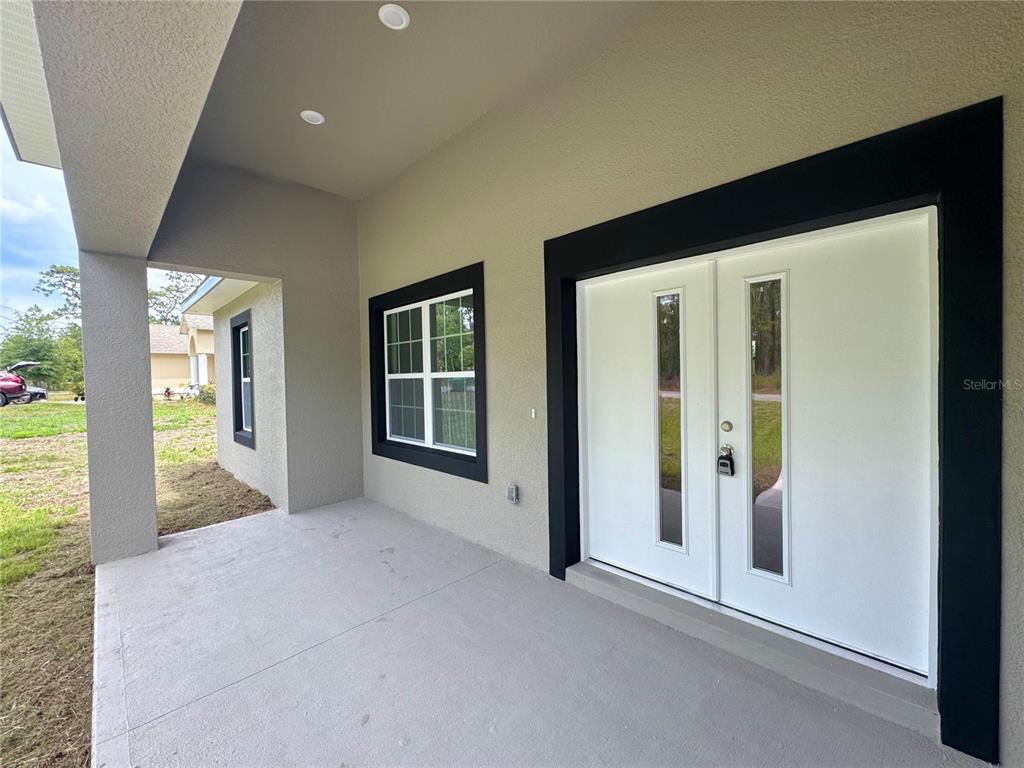 A covered concrete porch features a white double door with glass panels and black trim — 628 W HERONSBILL LANE, DUNNELLON, FL