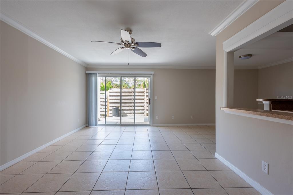 An empty living room with beige tile flooring, a ceiling fan, and sliding glass doors — 6860 WHITMAN COURT UNIT 32B, SARASOTA, FL