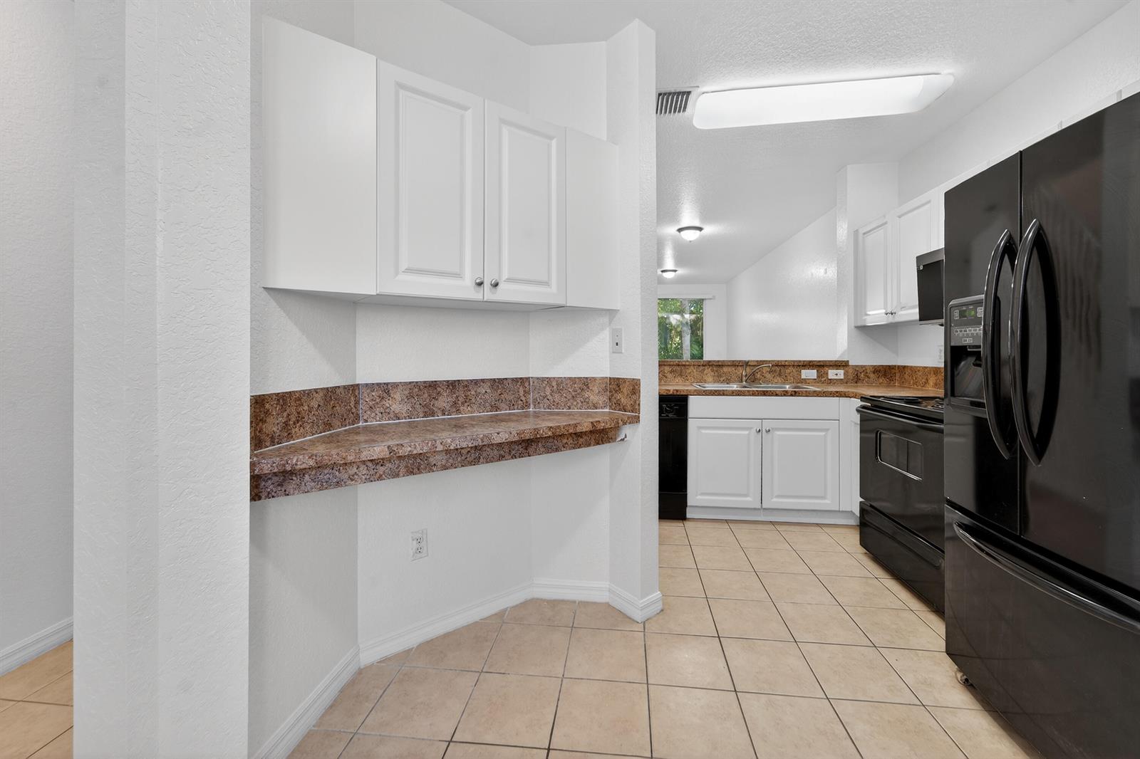 A kitchen features white cabinets, brown laminate countertops, black appliances, and beige tile flooring — 3635 Sonoma Drive, Riviera Beach FL 33404, RIVIERA BEACH, FL