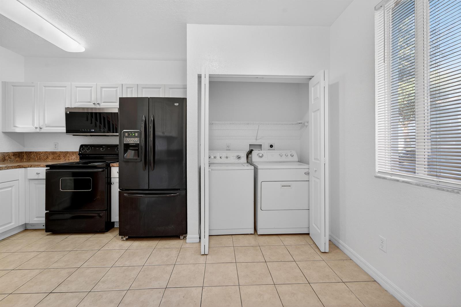 A kitchen features white cabinets, black appliances, a tiled floor, and a laundry closet — 3635 Sonoma Drive, Riviera Beach FL 33404, RIVIERA BEACH, FL