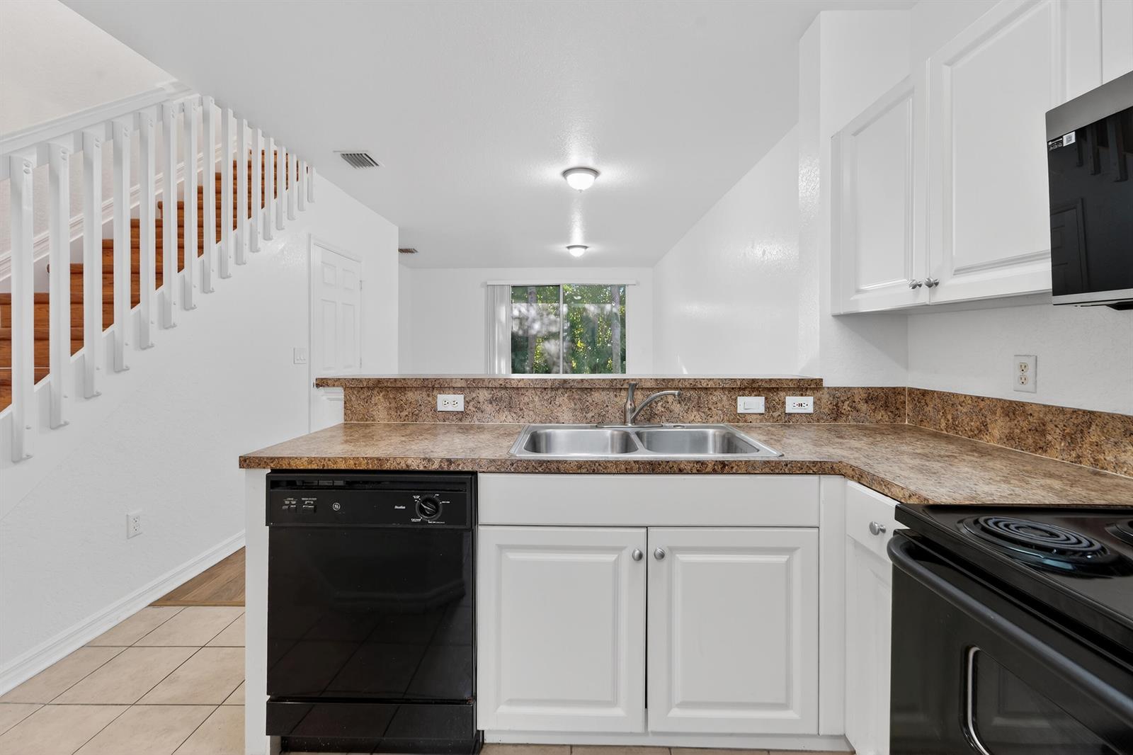A kitchen with white cabinets, black appliances, and brown laminate countertops overlooks a living area — 3635 Sonoma Drive, Riviera Beach FL 33404, RIVIERA BEACH, FL