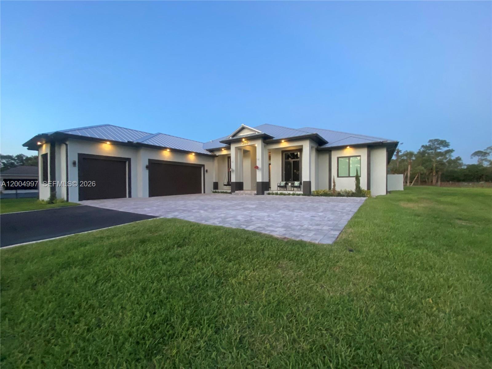A modern single-story house features a metal roof, a paved driveway, and a three-car garage — 360 13th St SW, Naples FL 34117, NAPLES, FL