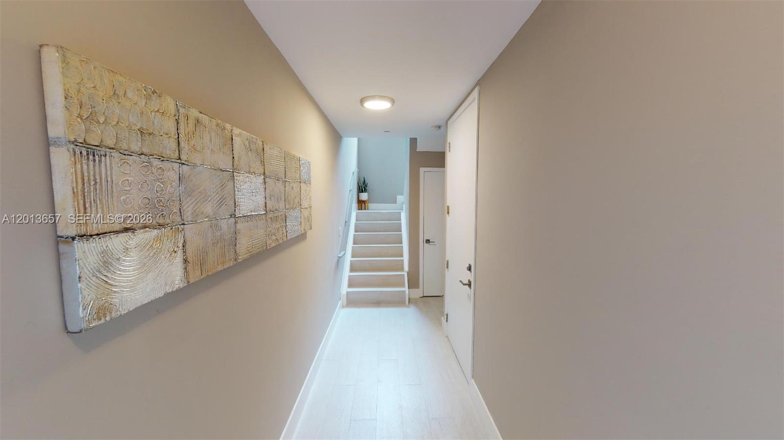 A hallway with light-colored flooring leads to a staircase with a small plant — FORT LAUDERDALE, FL