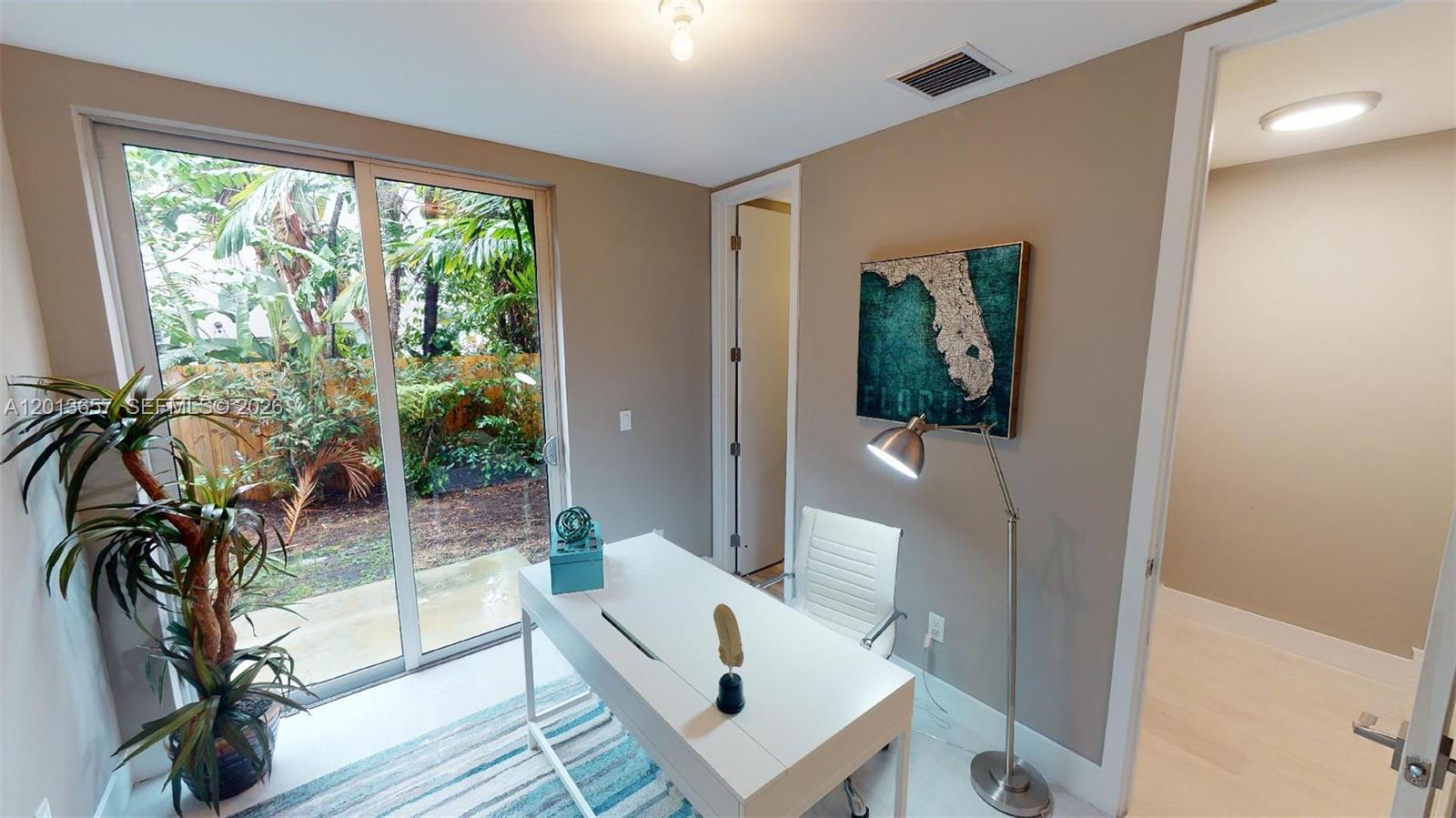 A home office features a white desk, a floor lamp, and sliding glass doors — FORT LAUDERDALE, FL