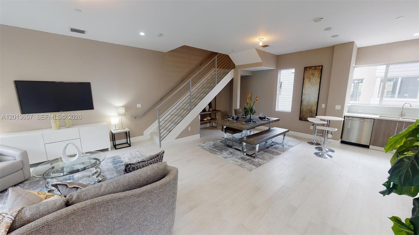 An open-concept living and dining area features light wood flooring, a staircase, and modern furniture — FORT LAUDERDALE, FL
