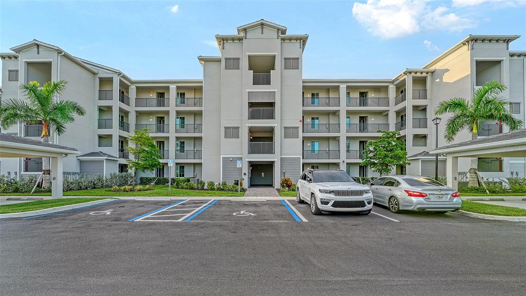 A multi-story apartment building exterior with a parking lot and two cars in front — 12140 WELLEN GOLF STREET UNIT 306, VENICE, FL