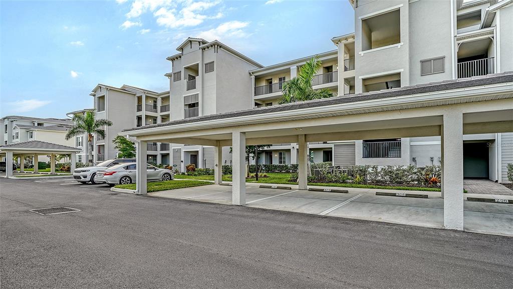 A covered parking area sits in front of a multi-story apartment building with palm trees — 12140 WELLEN GOLF STREET UNIT 306, VENICE, FL