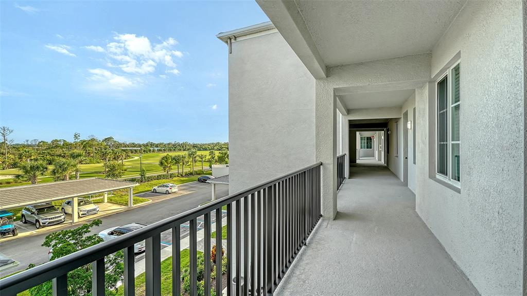An outdoor covered walkway overlooks a parking lot and a green landscape — 12140 WELLEN GOLF STREET UNIT 306, VENICE, FL