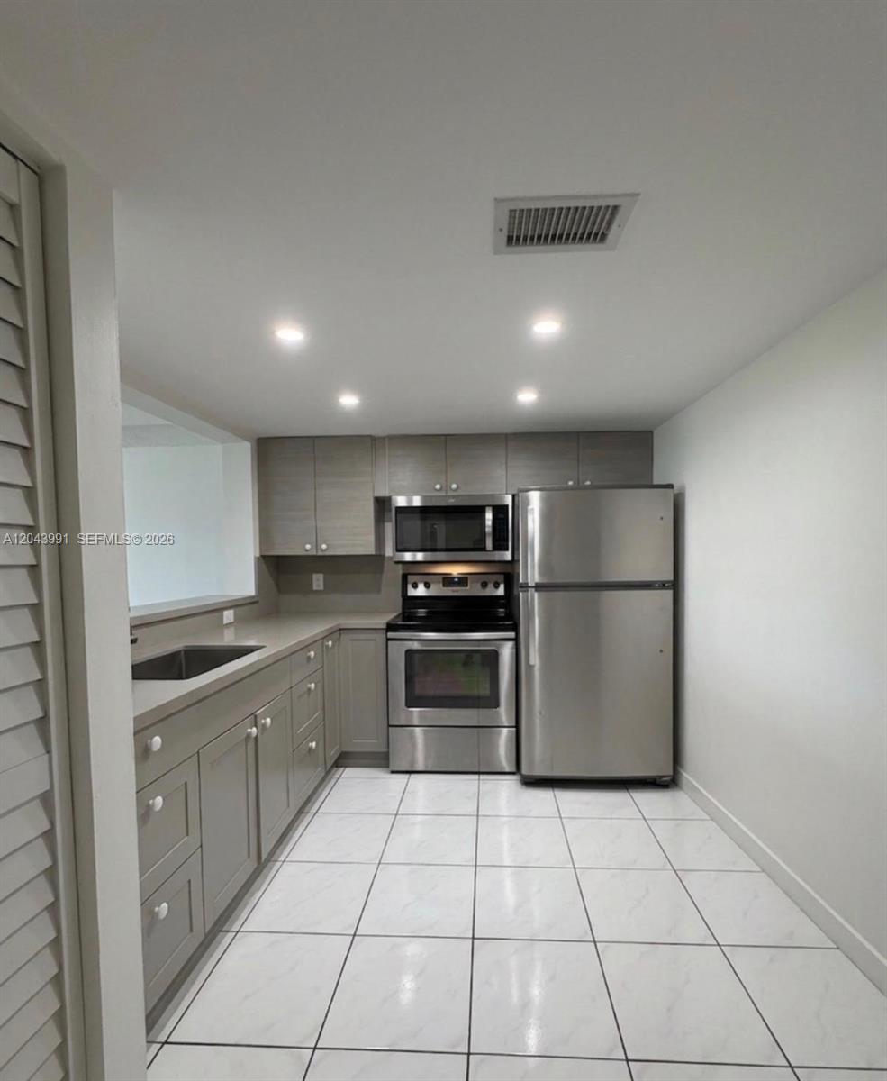 A kitchen features gray cabinets, stainless steel appliances, and white tiled flooring — 2055 SW 122nd Ave # 327, Miami FL 33175, MIAMI, FL