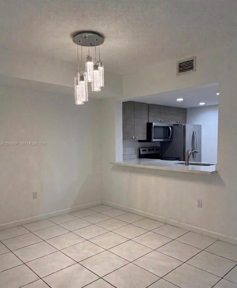 A dining area with a modern pendant light fixture overlooks a kitchen with stainless appliances — 2055 SW 122nd Ave # 327, Miami FL 33175, MIAMI, FL