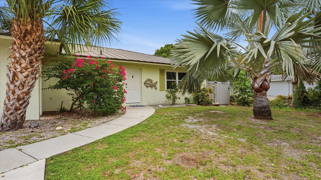 A light-colored house exterior features a metal roof, a palm tree, and a walkway — 6233 ROCKEFELLER AVENUE, SARASOTA, FL