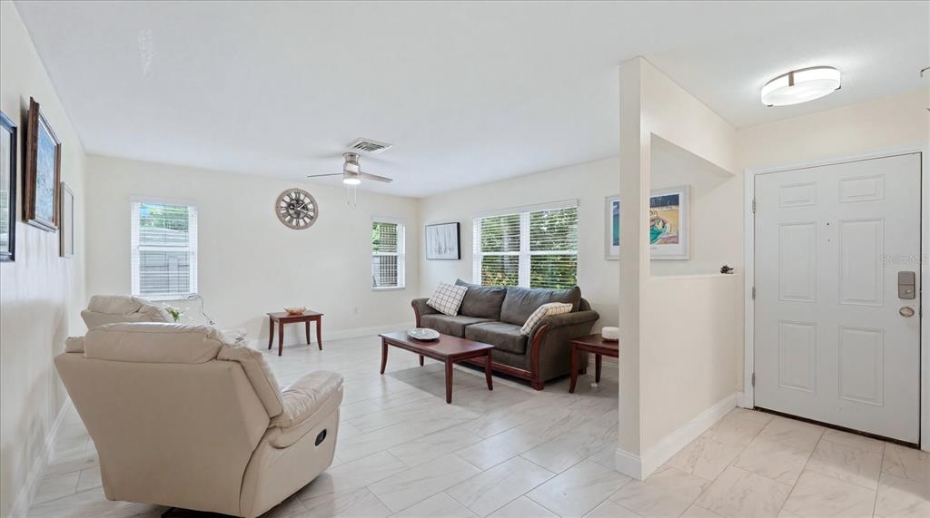 A living room with light tile floors, a sofa, a recliner, and a front door — 6233 ROCKEFELLER AVENUE, SARASOTA, FL