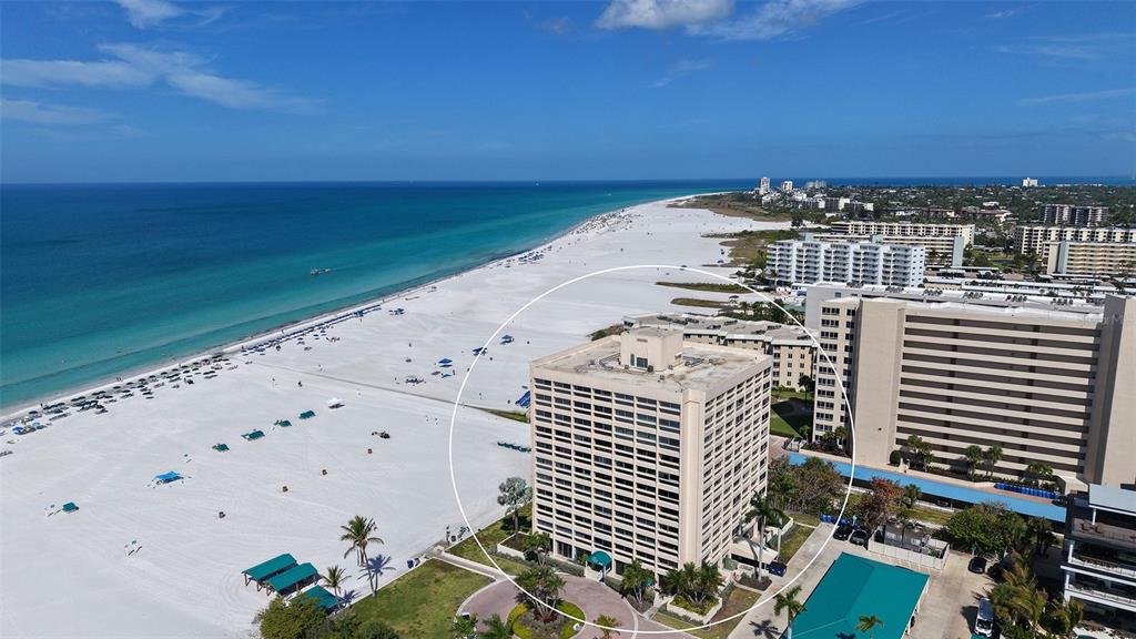 An aerial view shows a tall, beige residential building situated directly on a sandy beach — 5966 MIDNIGHT PASS ROAD UNIT G-67, SARASOTA, FL