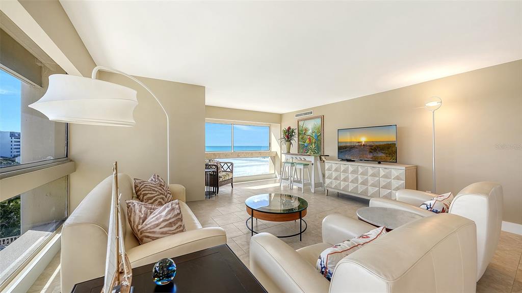 A bright living room features light-colored furniture, tile flooring, and a large window overlooking the ocean — 5966 MIDNIGHT PASS ROAD UNIT G-67, SARASOTA, FL