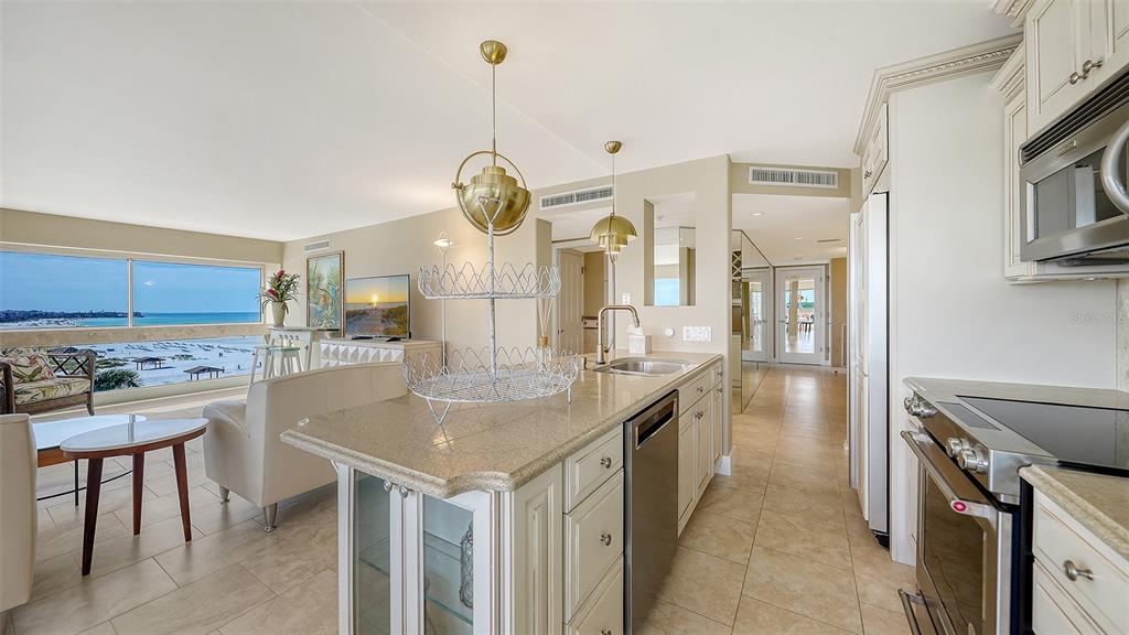 A kitchen with granite countertops and stainless steel appliances overlooks a living area and beach — 5966 MIDNIGHT PASS ROAD UNIT G-67, SARASOTA, FL