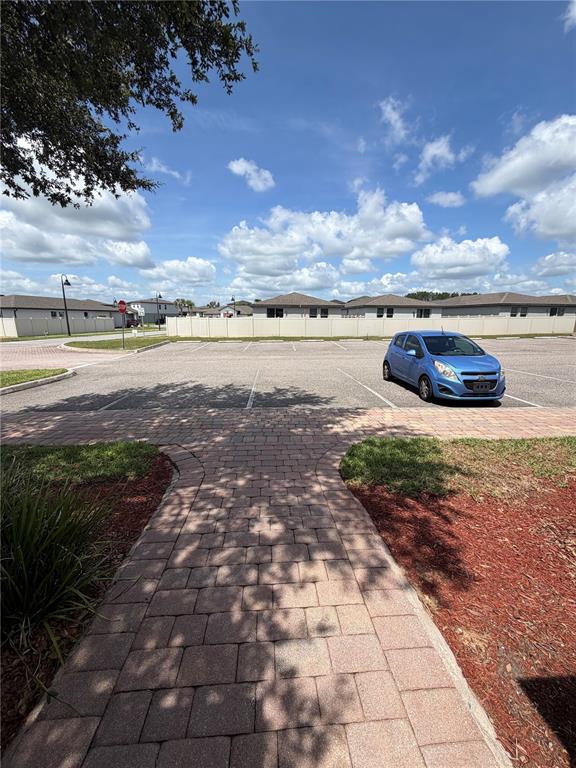 A paved walkway leads to a parking lot with a blue car and residential buildings — 2404 BELLA VISTA DRIVE, DAVENPORT, FL