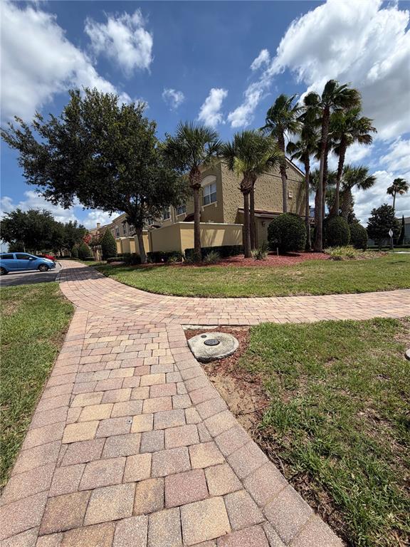 A paved walkway leads toward a multi-story tan building surrounded by palm trees and landscaping — 2404 BELLA VISTA DRIVE, DAVENPORT, FL