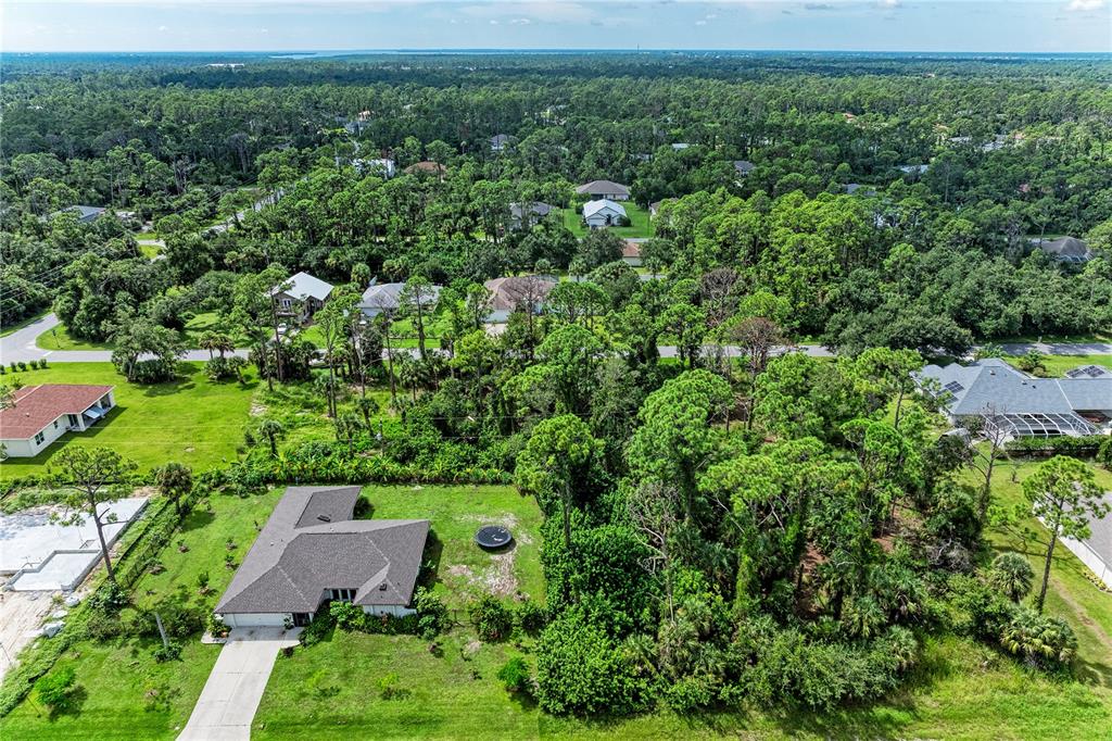 An aerial view shows a residential property with a house, surrounding trees, and nearby homes — 15106 GULISTAN AVENUE, PORT CHARLOTTE, FL
