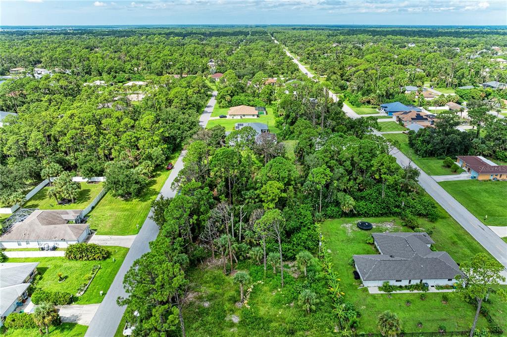 An aerial view shows a vacant, wooded residential lot situated between two houses and roads — 15106 GULISTAN AVENUE, PORT CHARLOTTE, FL