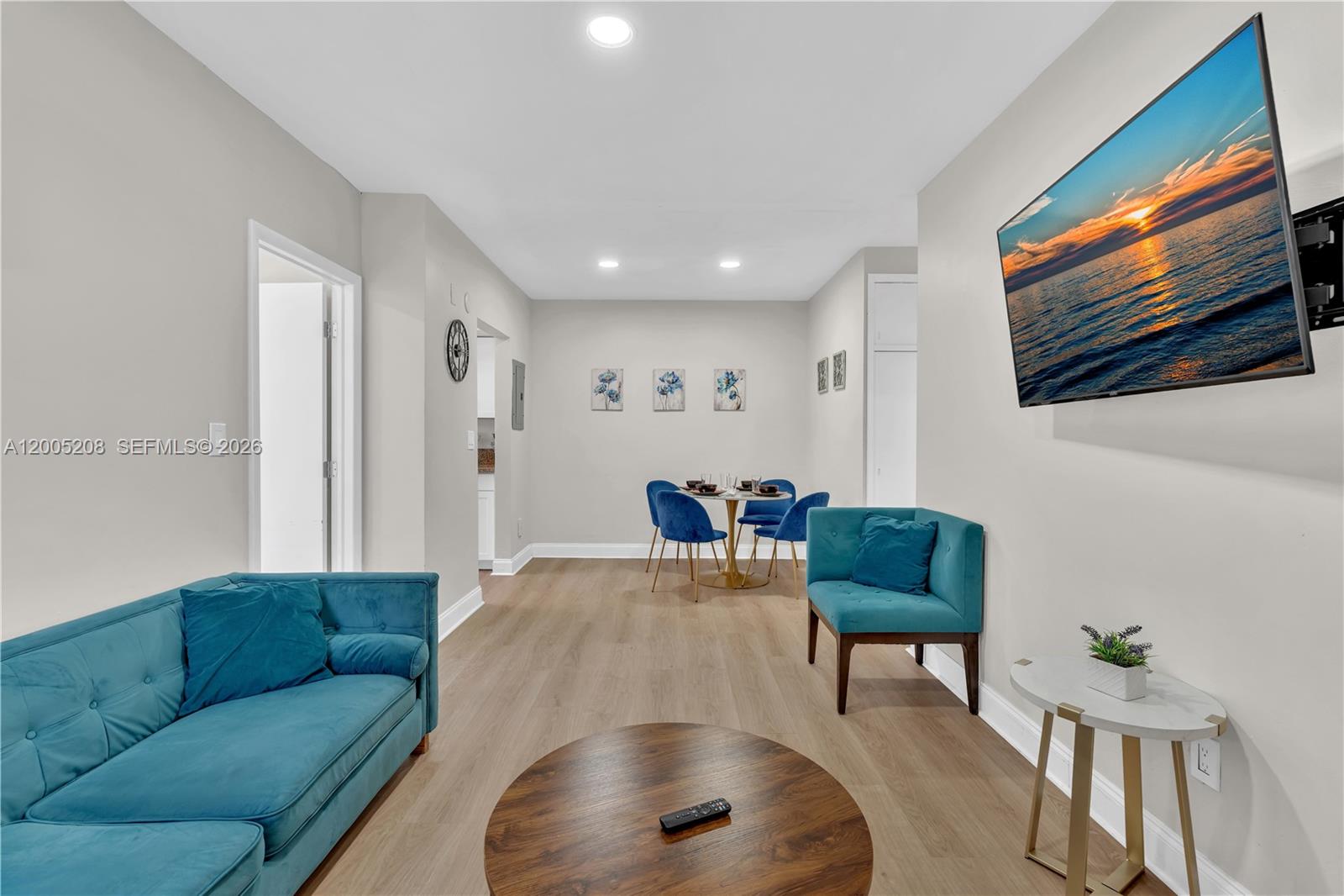 This living and dining area features teal furniture, light wood flooring, and a wall-mounted television — 10006 E Bay Harbor Dr # 11, Bay Harbor Islands FL 33154, BAY HARBOR ISLANDS, FL