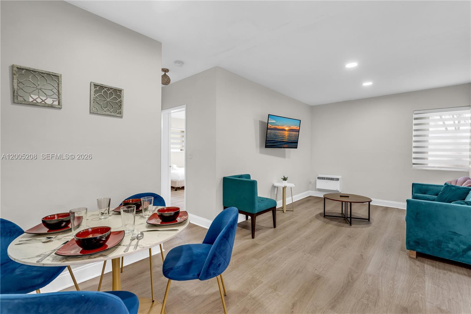 This open-concept living and dining area features wood-look flooring, blue velvet furniture, and a television — 10006 E Bay Harbor Dr # 11, Bay Harbor Islands FL 33154, BAY HARBOR ISLANDS, FL