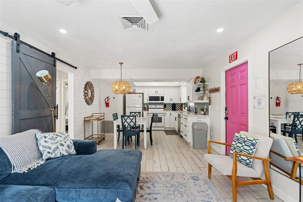 An open-concept living room and kitchen featuring a blue sectional, dining area, and pink door — 8106 GULF DRIVE UNIT A&B, HOLMES BEACH, FL