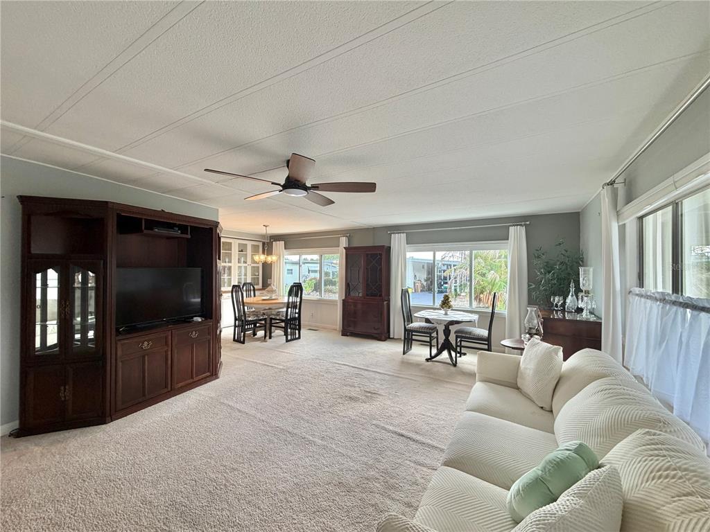 A living room with beige carpet, a large wooden entertainment center, and two dining areas — 101 TAMARISK WAY, LEESBURG, FL