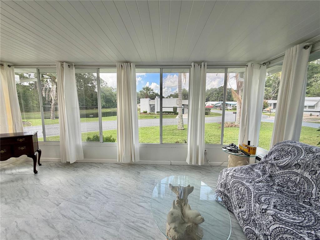 A sunroom with white tile flooring, large windows, and white curtains overlooking a grassy area — 101 TAMARISK WAY, LEESBURG, FL