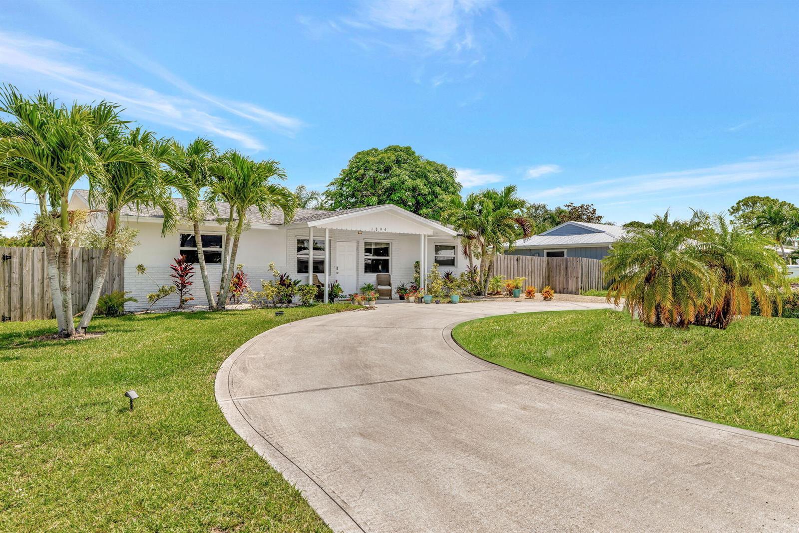 A white single-story house features a curved concrete driveway and several palm trees — 1894 SE Lafayette Street, Stuart FL 34997, STUART, FL