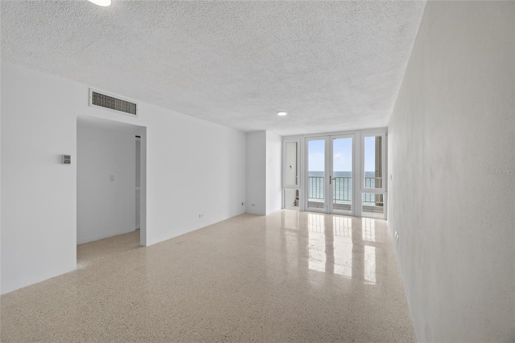 An empty room with light-colored terrazzo flooring, beige walls, and a glass door to a balcony — 3409 AVE. ISLA VERDE UNIT 704, CAROLINA, PR