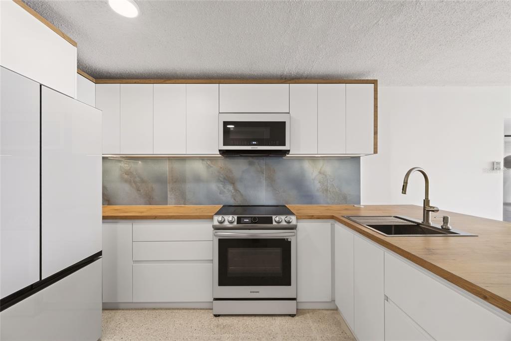 A kitchen features white cabinets, wood-tone countertops, a marble-patterned backsplash, and stainless steel appliances — 3409 AVE. ISLA VERDE UNIT 704, CAROLINA, PR
