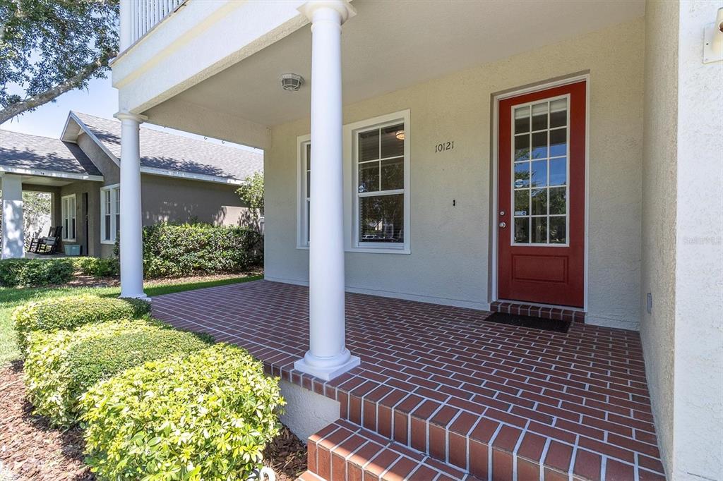 A covered front porch features brick flooring, white columns, and a red front door — 10121 PORCH STREET, NEW PORT RICHEY, FL