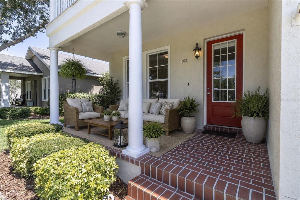 A covered front porch features a brick floor, wicker furniture, and a red front door — 10121 PORCH STREET, NEW PORT RICHEY, FL