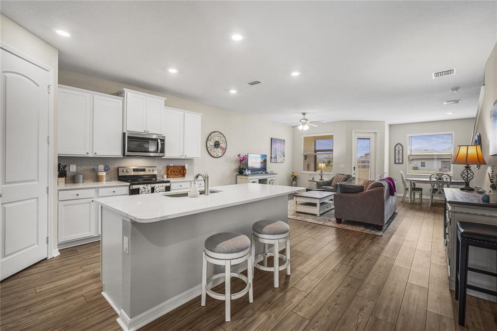 An open-concept kitchen with white cabinets and a center island overlooks a living area — 11240 CAY SPRUCE WAY, SAN ANTONIO, FL