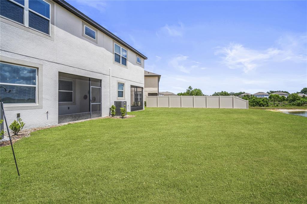 A view of a backyard with a grassy lawn, a beige house, and a privacy fence — 11240 CAY SPRUCE WAY, SAN ANTONIO, FL