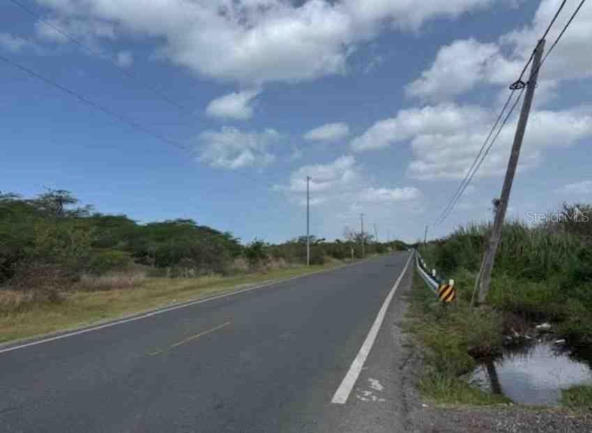 A paved road stretches into the distance past a utility pole and a roadside ditch — SR-1, KM. 109.9 RÍO CAÑAS ABAJO, JUANA DIAZ, PR