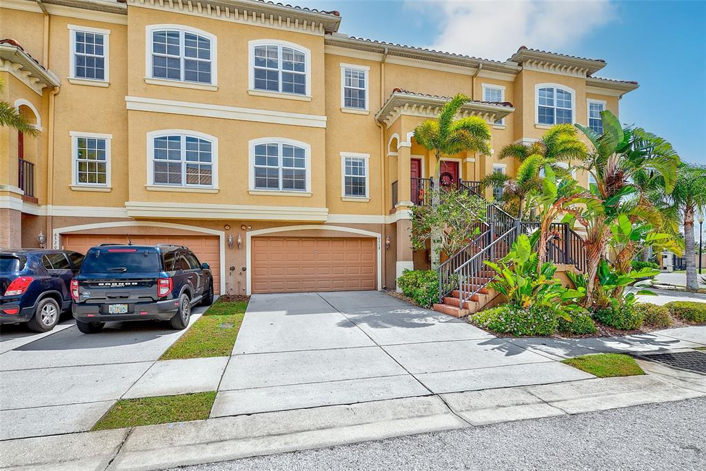 A three-story yellow townhouse with two garage doors and an exterior staircase leading to entrances — 6518 SAND SHORE LANE, NEW PORT RICHEY, FL