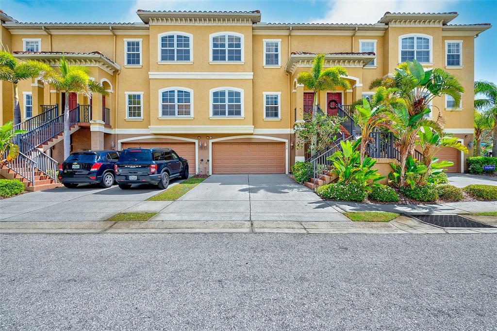 A multi-story yellow townhouse exterior with two garages, a driveway, and palm trees — 6518 SAND SHORE LANE, NEW PORT RICHEY, FL