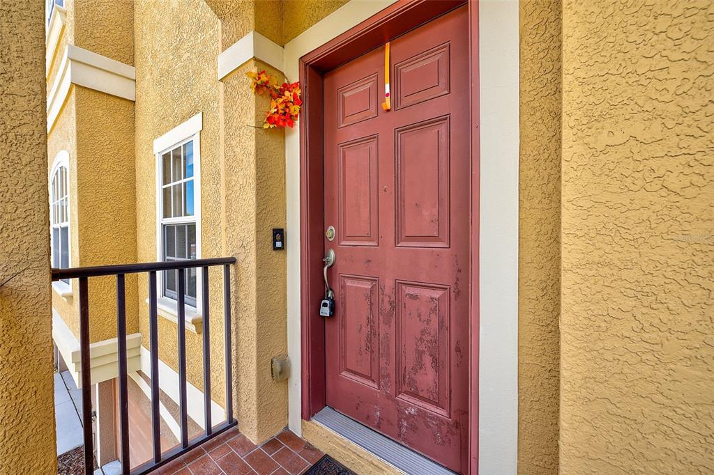 A weathered red front door with a lockbox sits on a tiled porch — 6518 SAND SHORE LANE, NEW PORT RICHEY, FL