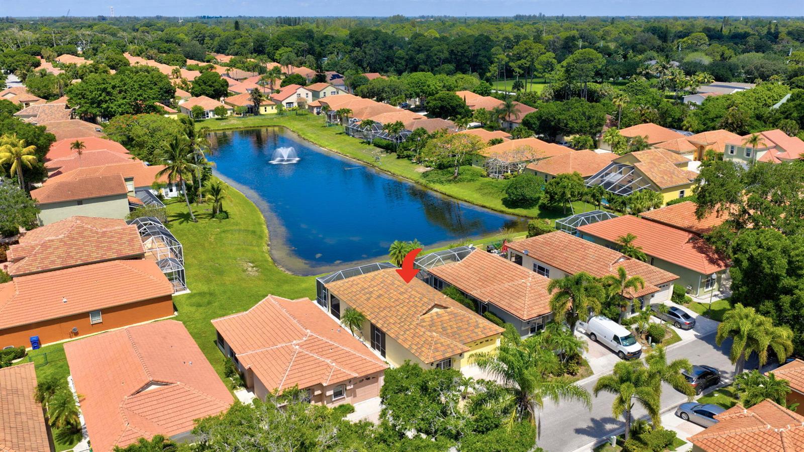 An aerial view shows a residential neighborhood with houses surrounding a central lake with fountains — 2097 Bonisle Circle, Riviera Beach FL 33418, RIVIERA BEACH, FL