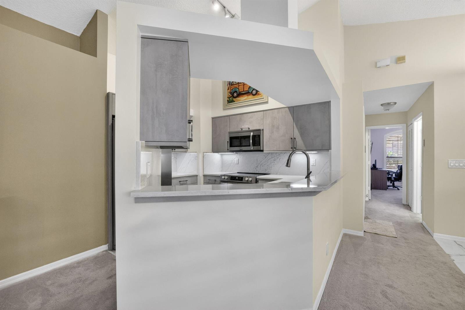 A modern kitchen features gray cabinets, stainless steel appliances, and white marble-style countertops and backsplash — 2097 Bonisle Circle, Riviera Beach FL 33418, RIVIERA BEACH, FL
