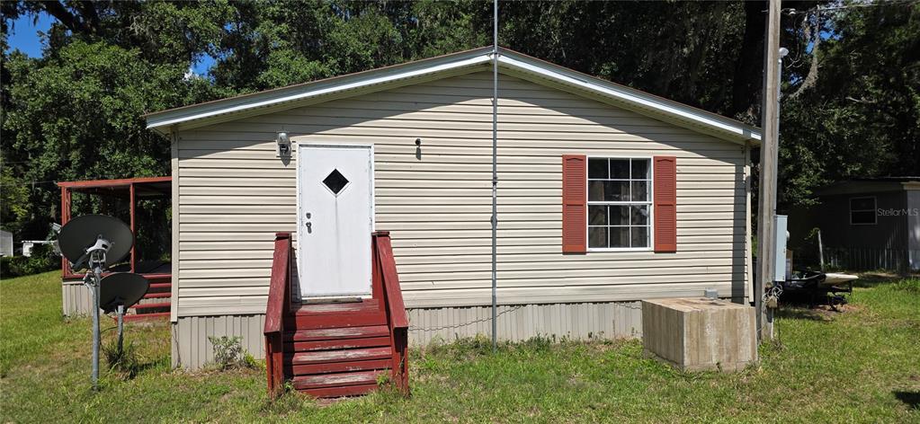 The exterior of a single-story house with beige siding, a red door, and red stairs — 11736 CR 675W, WEBSTER, FL