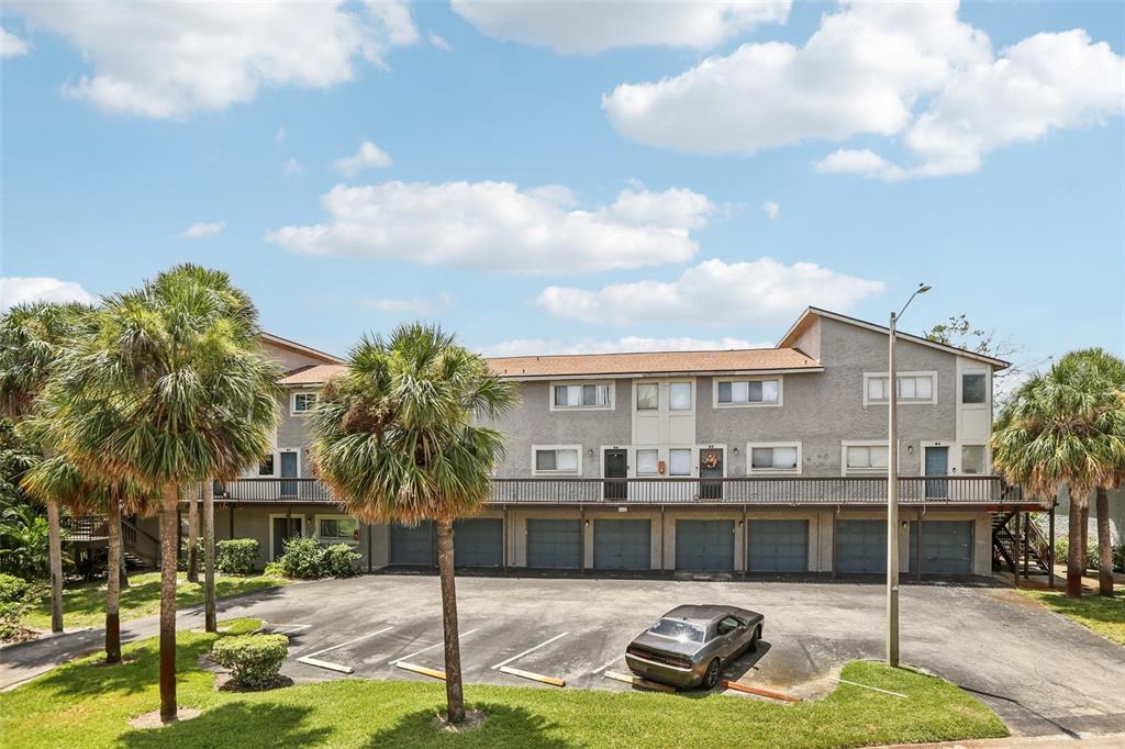 A multi-story apartment building features a ground-level parking garage, a balcony, and palm trees — 6325 NEWTOWN CIRCLE UNIT 25B2, TAMPA, FL