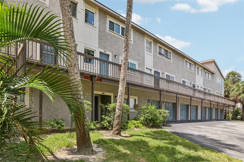 A multi-story apartment building features a second-floor balcony, ground-level garages, and palm trees — 6325 NEWTOWN CIRCLE UNIT 25B2, TAMPA, FL
