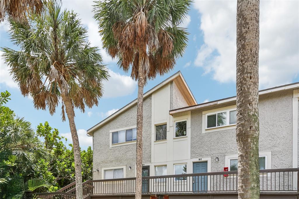 A two-story townhouse exterior features gray stucco siding, a wooden deck, and tall palm trees — 6325 NEWTOWN CIRCLE UNIT 25B2, TAMPA, FL