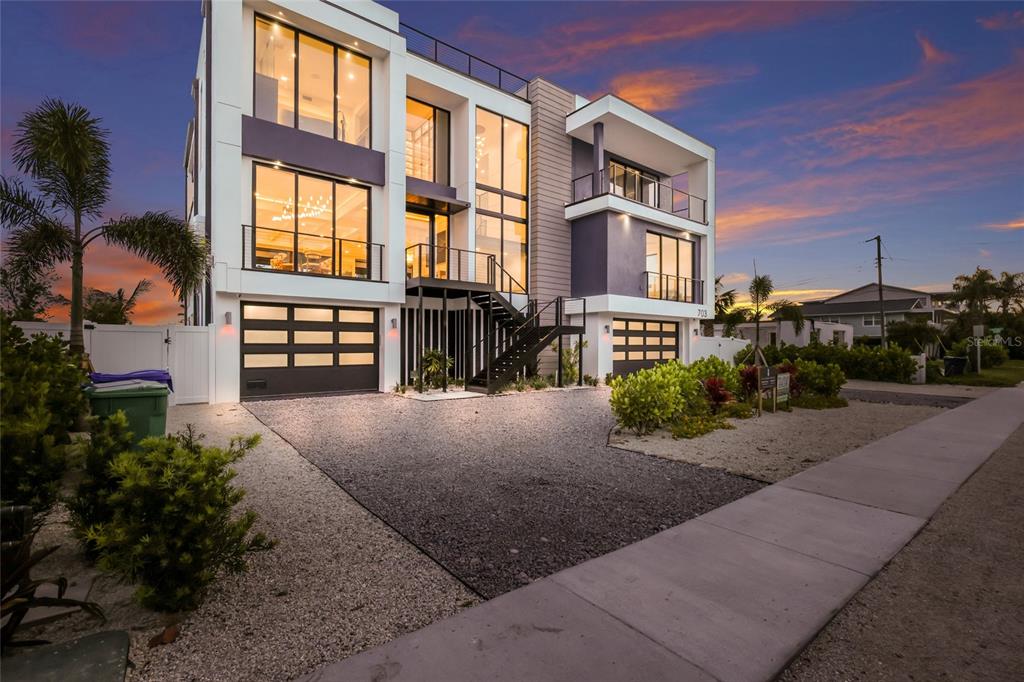 A modern three-story house with large windows, a gravel driveway, and an exterior staircase — 703 S BAY BOULEVARD, ANNA MARIA, FL