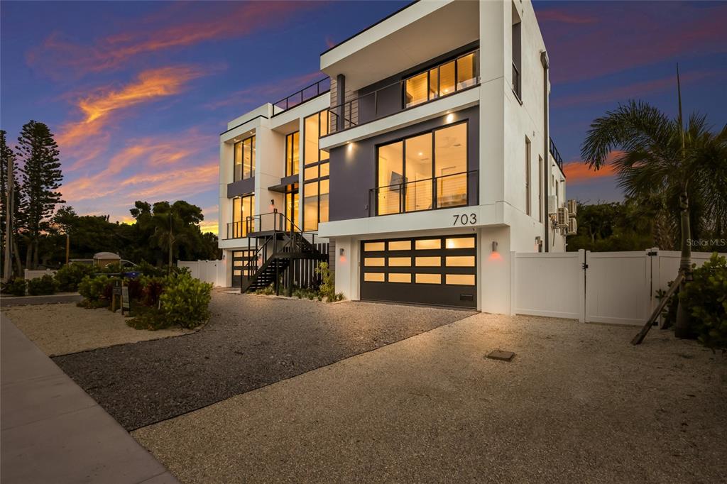 A modern three-story house with a gravel driveway, garage, and balconies at sunset — 703 S BAY BOULEVARD, ANNA MARIA, FL