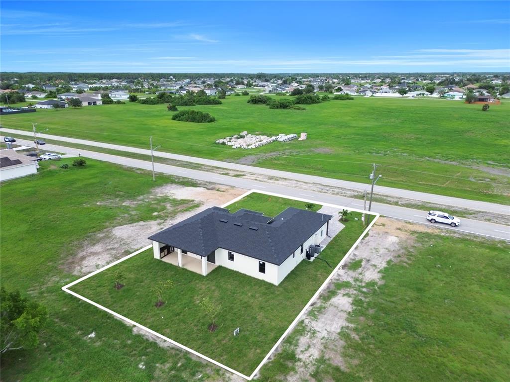 An aerial view shows a white, L-shaped house with a dark roof on a grassy lot — 2720 SANTA BARBARA BOULEVARD N, CAPE CORAL, FL